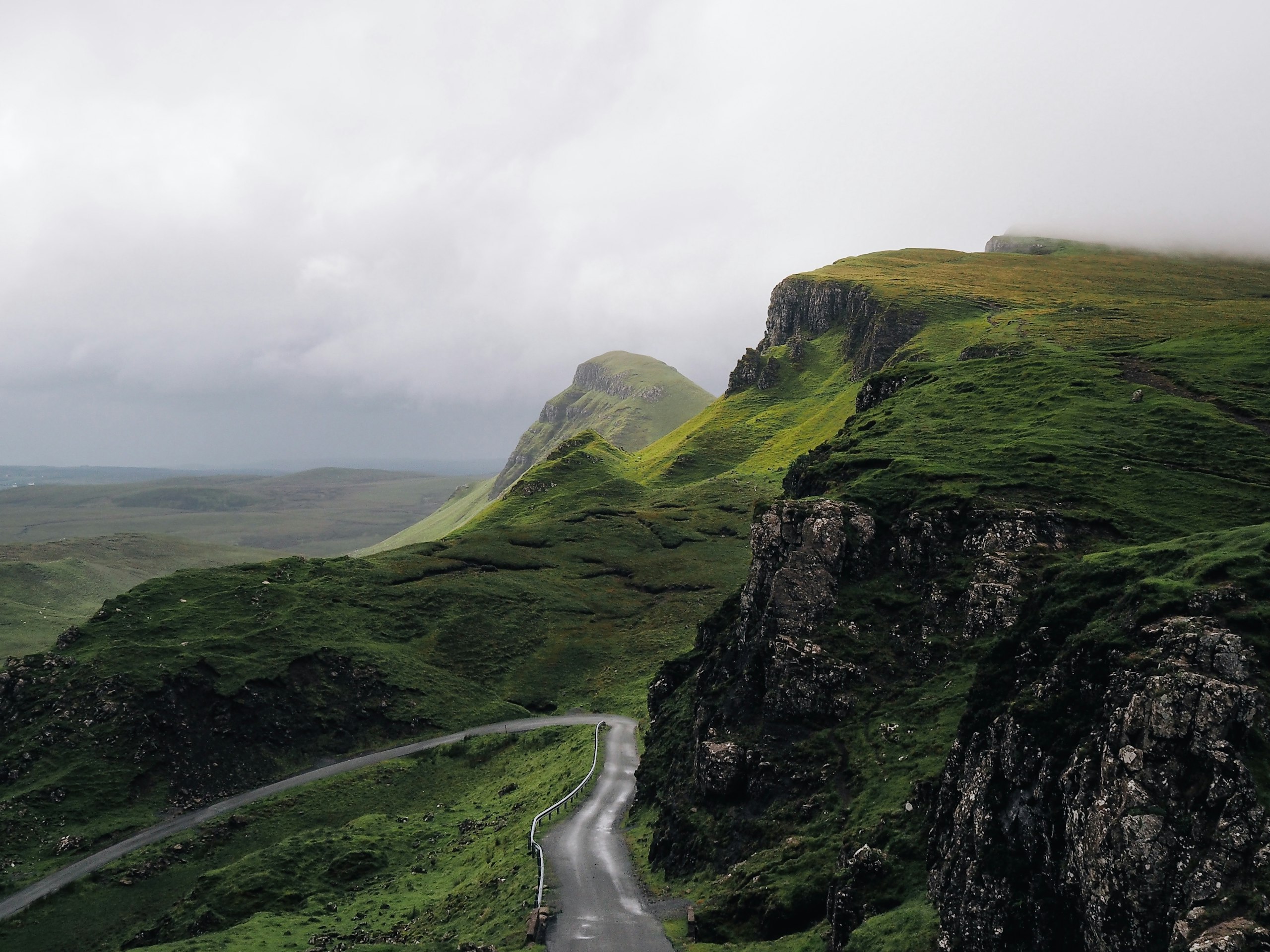 An empty road winding between green Irish mountains